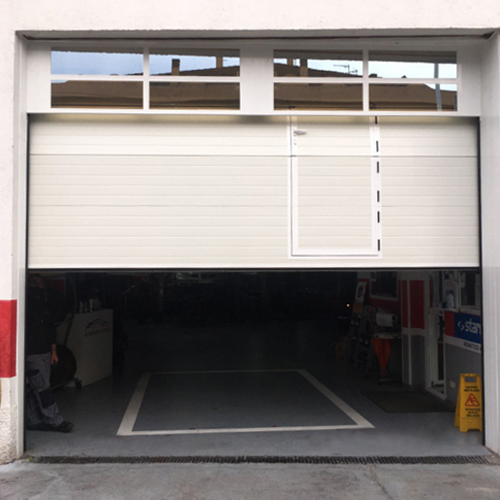 puerta seccional industrial con peatonal insertada y dintel acristalado
